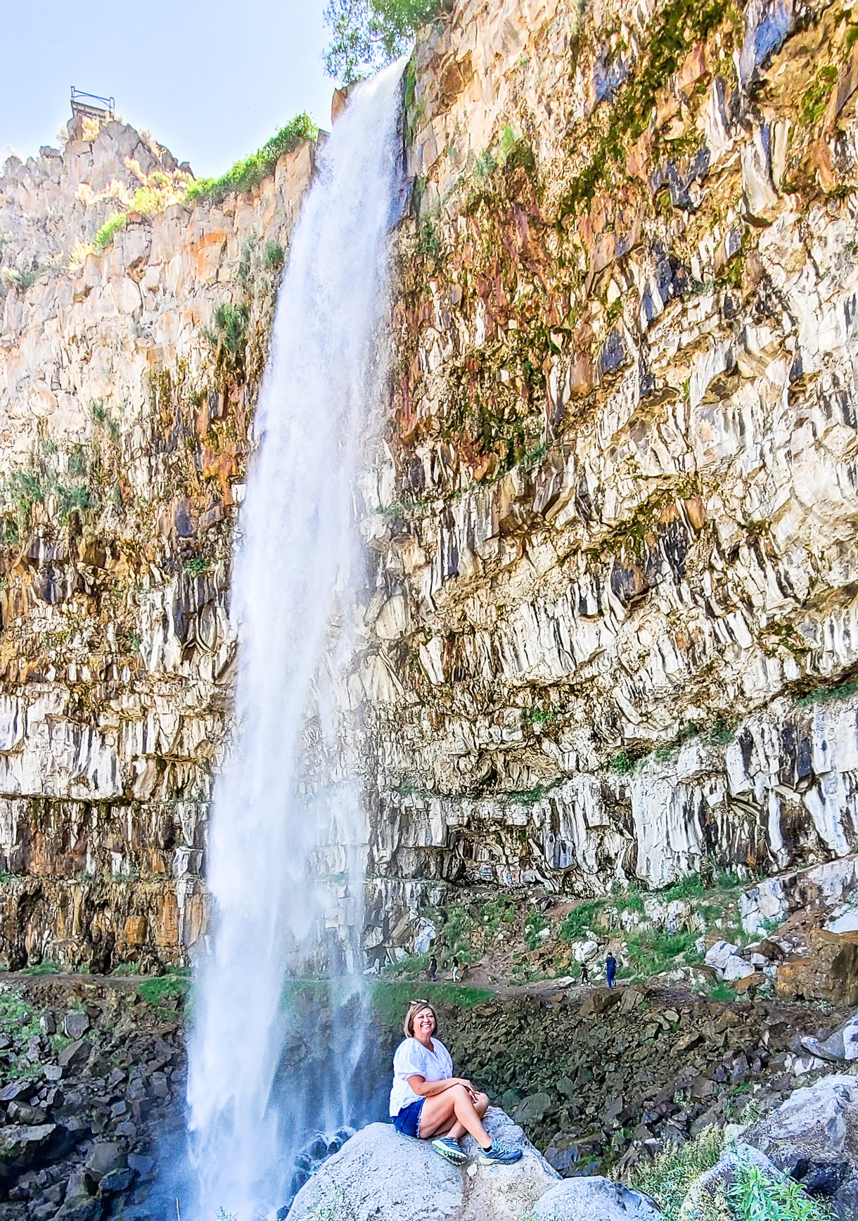 Woman sitting on a boulder in front of a waterfall