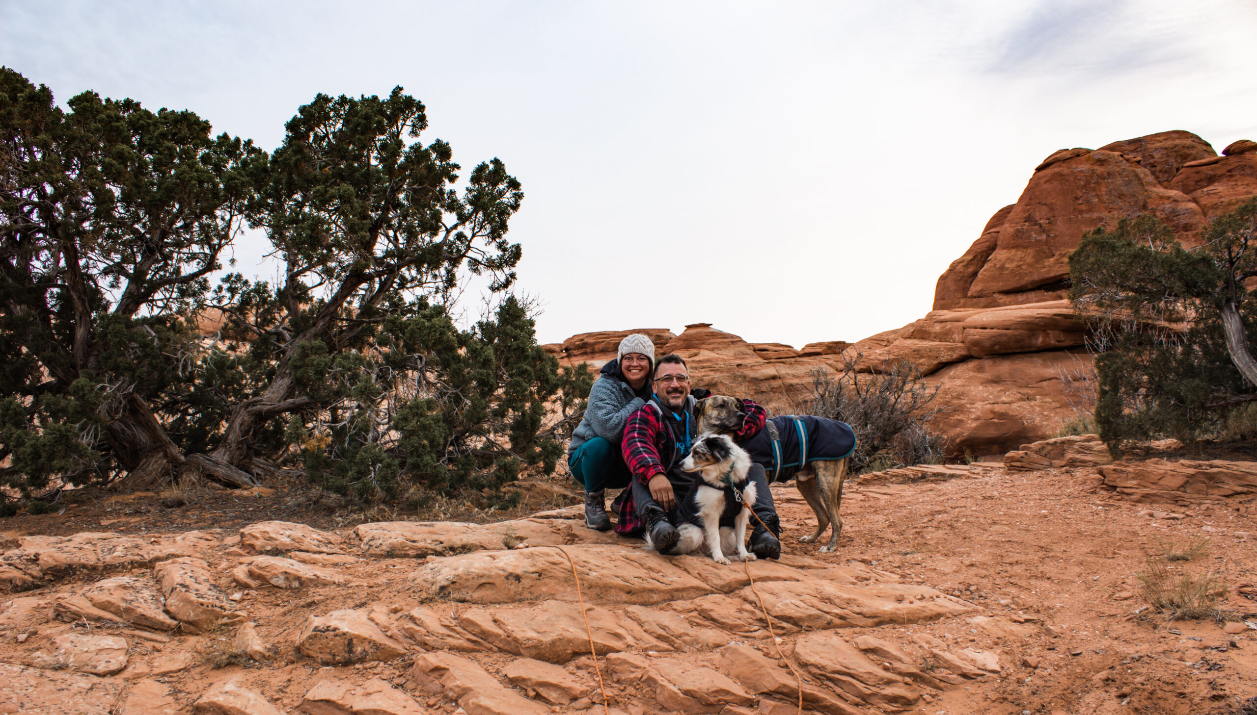 couple with their two dogs posing at Arches National Park at a campground site. They are dressed warmly because it is December.